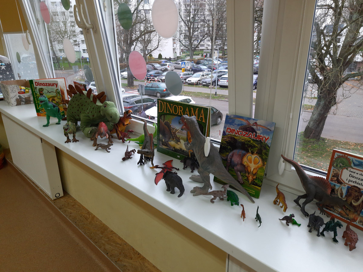 Grafika przedstawia eksponaty przyniesione przez uczniów kl. 1a na lekcjeo prehistorii m.in. figurki dinozaurów