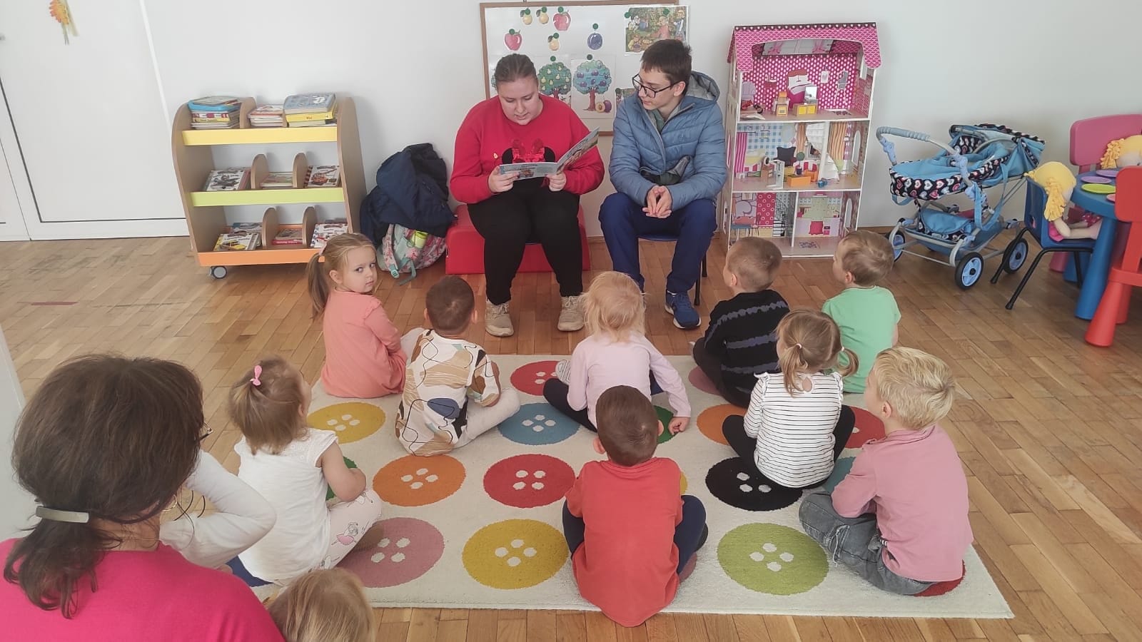 Uczniowie czytają książkę przedszkolakom.