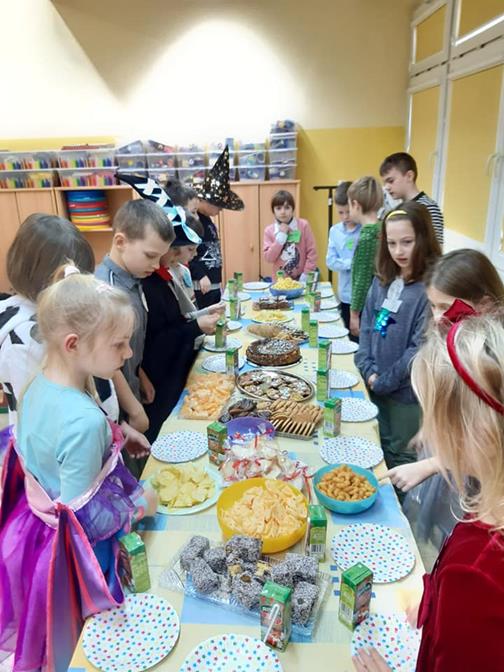 uczniowie w przebraniach stoją przy stole zastawionym jedzeniem 
