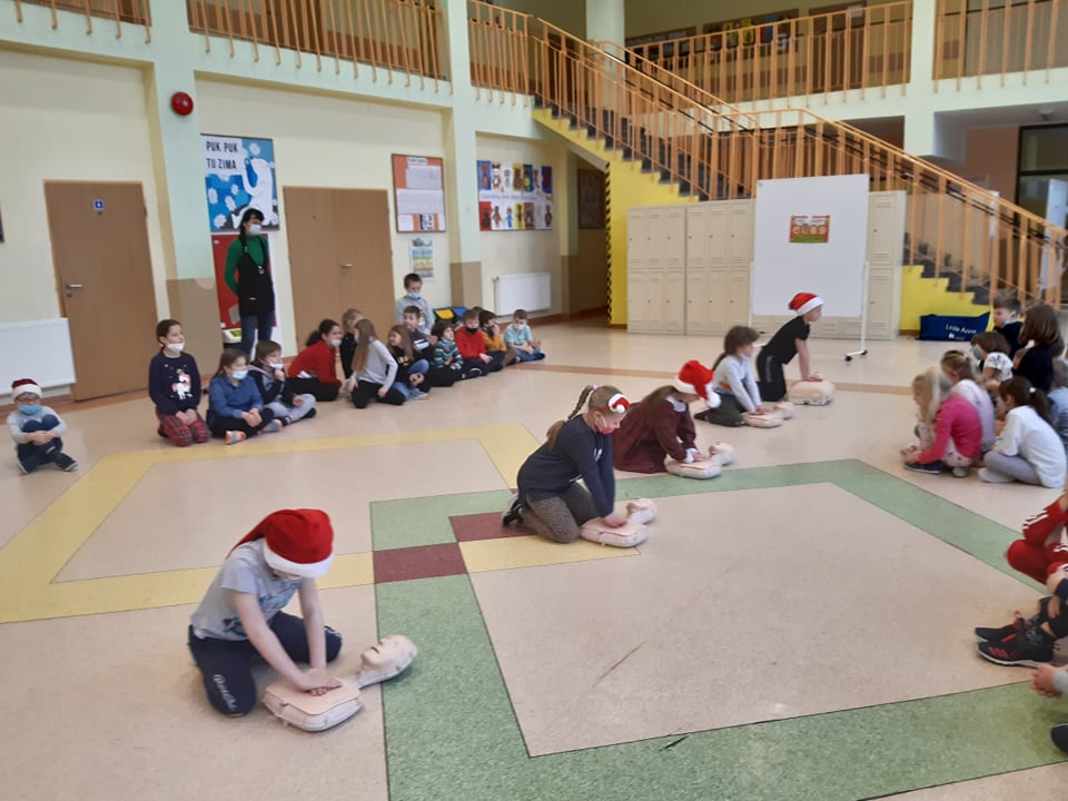 Dzieci ćwiczą masaż serca na fantomach rozłożonych na holu szkolnym