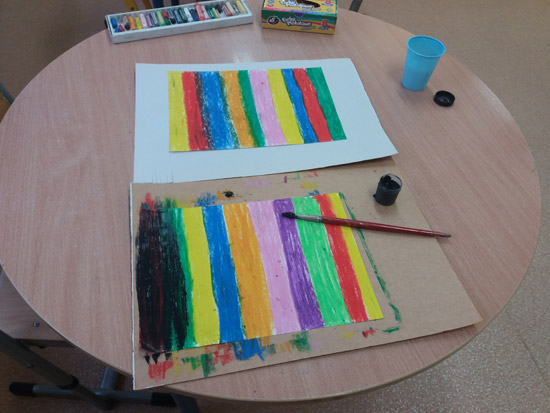 Grafika przedstawia dwie kartki z bloku pomalowane w paski kolorowymi pastelami. Jedna z kartek pokryta jest w części czarna farbą