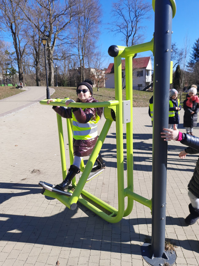 Grafika przedstawia ucznia z klasy 1a na przyrządzie do ćwiczeń w parku