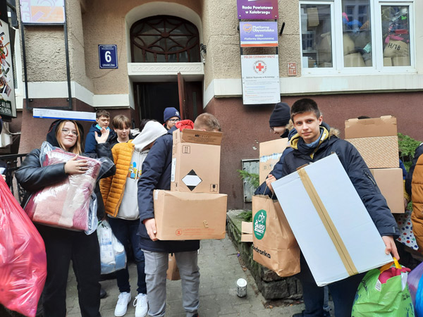 Grafika przedstawia uczniów z klasy 8c przed wejściem do Kołobrzeskiego koła PCK z darami zebranymi na pomoc Ukrainie