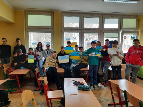 Grafika przedstawia uczniów z klasy 8c w sali lekcyjnej z flagami Ukrainy
