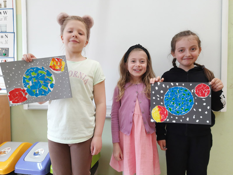 Grafika przedstawia dzieci z koła plastycznego prezentujące  prace wykonane z okazji Dnia Ziemi