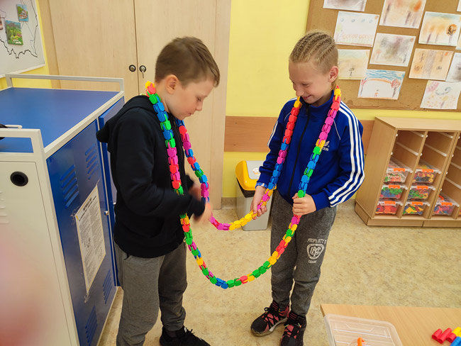Na zdjęciu dwóch uczniów z klasy 3a z łańcuchem na szyi wykonanym z klockó
