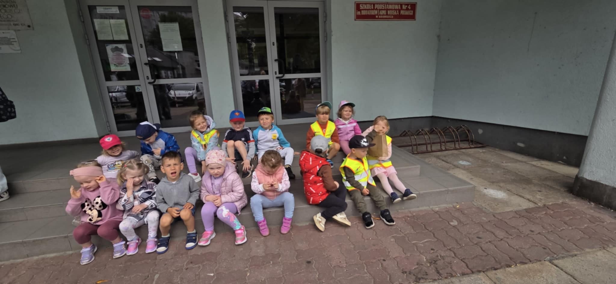 Dzieci siedzą przed szkołą.
